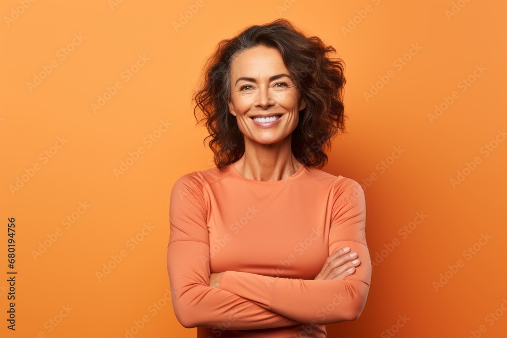 Fototapeta premium Portrait of a glad woman in her 50s showing off a lightweight base layer against a soft orange background. AI Generation