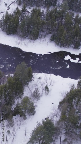 Aerial view of a white winter landscape with a frozen river in the mountains with  flowing water in North Canada (ID: 680200925)