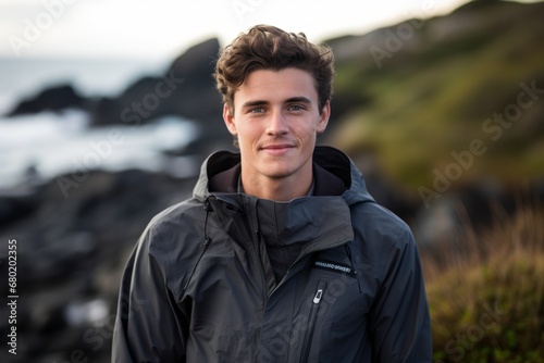 Portrait of a blissful man in his 20s wearing a windproof softshell against a rocky shoreline background. AI Generation