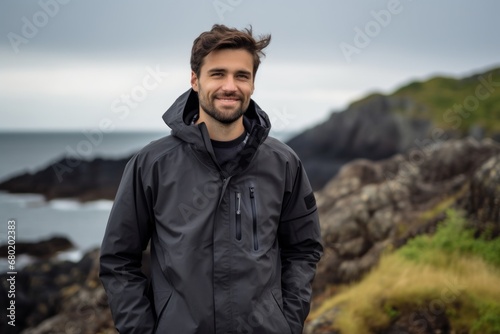 Portrait of a blissful man in his 20s wearing a windproof softshell against a rocky shoreline background. AI Generation