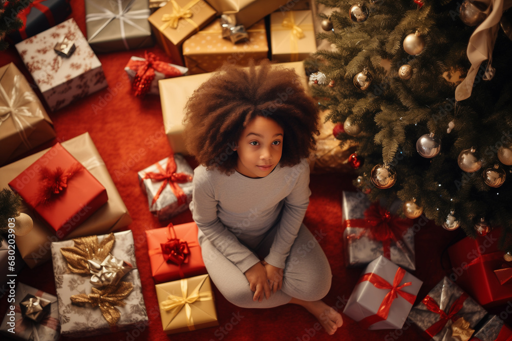 A young African-American girl sits by a Christmas tree surrounded by presents A young African-American girl sits by a Christmas tree surrounded by presents