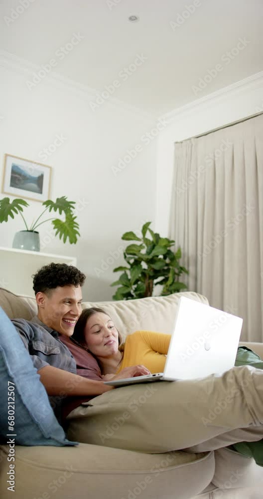 Vertical video of happy diverse couple sitting on sofa using laptop at home, in slow motion Vertical video of happy diverse couple sitting on sofa using laptop at home, in slow motion
