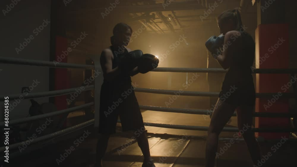 Long shot of trainer teaching woman to do boxing stance at dimly lit ring Long shot of trainer teaching woman to do boxing stance at dimly lit ring