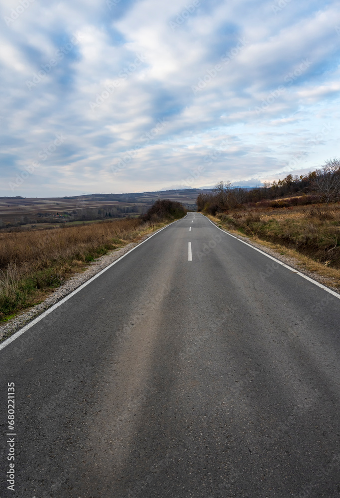 New country road in autumn.  Country road cutting through green fields in the countryside. Empty asphalt road in rural landscape with dramatic clouds. Open Road.  