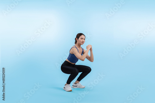 Vigorous energetic woman doing exercise. Young athletic asian woman strength and endurance training session as squat workout routine session. Full body studio shot on isolated background.