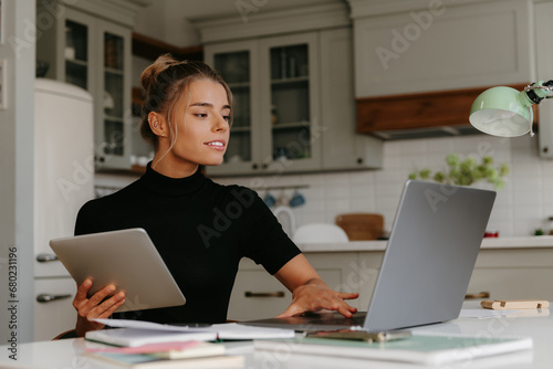 Confident young woman sitting at the desk and technologies while working at home © gstockstudio