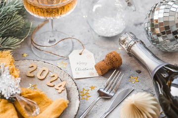 Table setting. Stylish plates, napkin, glass, champagne, Christmas tree branches and Christmas decorations on a gray background. The concept of merry Christmas and New Year 2024.