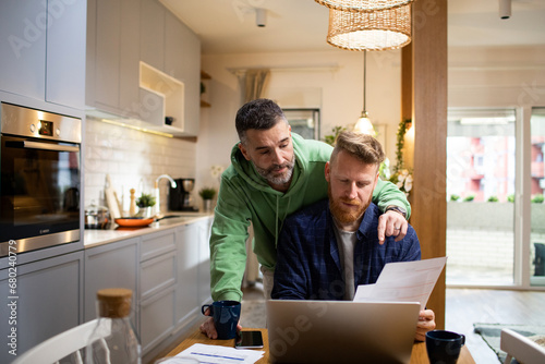 Gay couple discussing paperwork over coffee in their kitchen photo