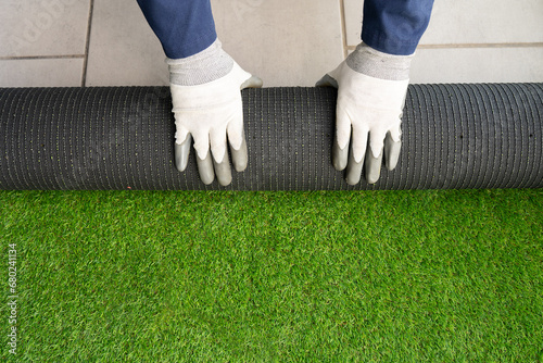 Men's hands holding a roll of artificial grass and installing it on a house. Artificial grass background. photo