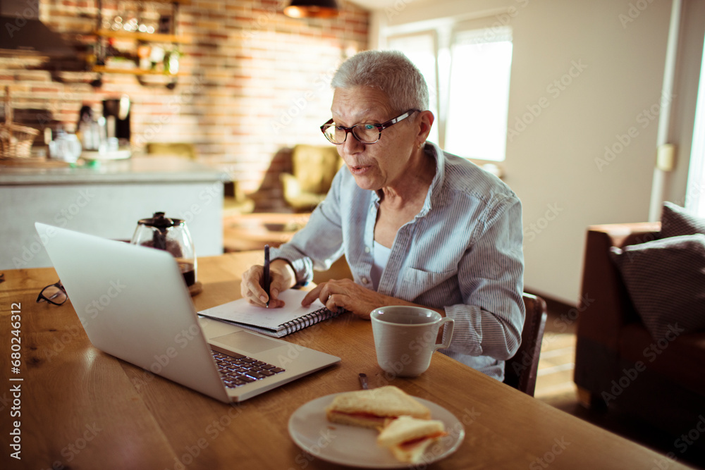 Senior woman working from home and taking notes Senior woman working from home and taking notes