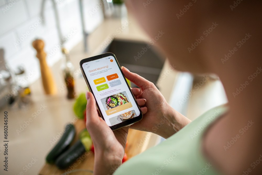 Young woman using recipe app on smartphone for preparing meal at home