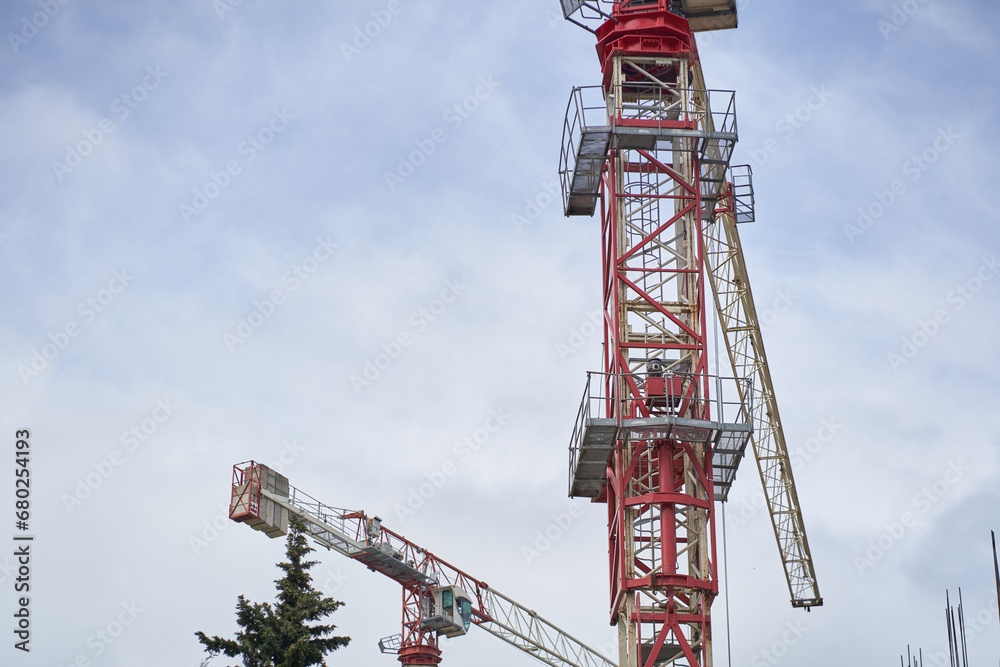Tower cranes near a building under construction against the background of the sky and white clouds. Construction concept. With space to copy. High quality photo Tower cranes near a building under construction against the background of the sky and white clouds. Construction concept. With space to copy. High quality photo