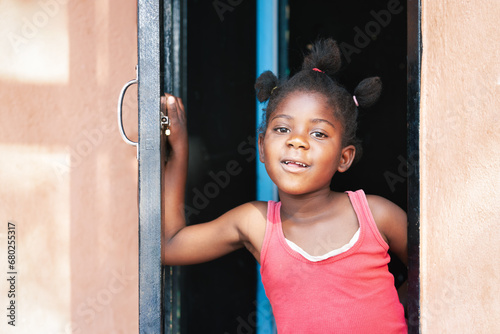 happy small african girl standing in the door frame in front of the house
