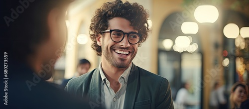 The stylish Italian man, sporting fashionable glasses, looks up with a smile as he finds himself in a close and happy interaction with the eye doctor in the education-filled interior, showcasing his photo