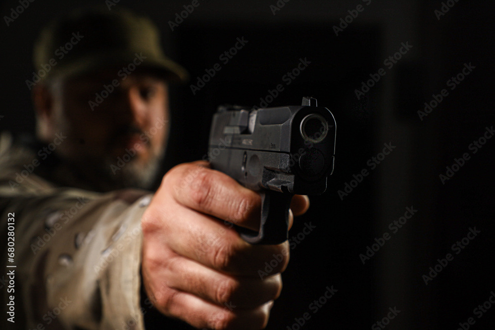 White man in coyote military outfit armed with a pistol on a black background
White man in coyote military outfit armed with a pistol on a black background