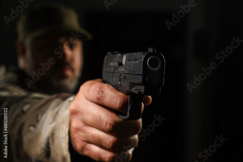  White man in coyote military outfit armed with a pistol on a black background