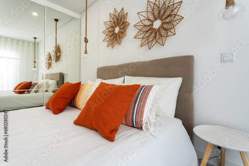 Double bed in the bright bedroom room interior furnishing furniture. Red decorative pillows and lamp shades in the foreground.