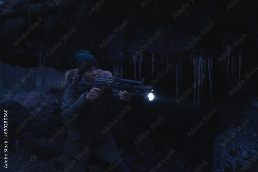 A girl with a rifle with a flashlight in the dark near a destroyed building in winter.  Low light photography.