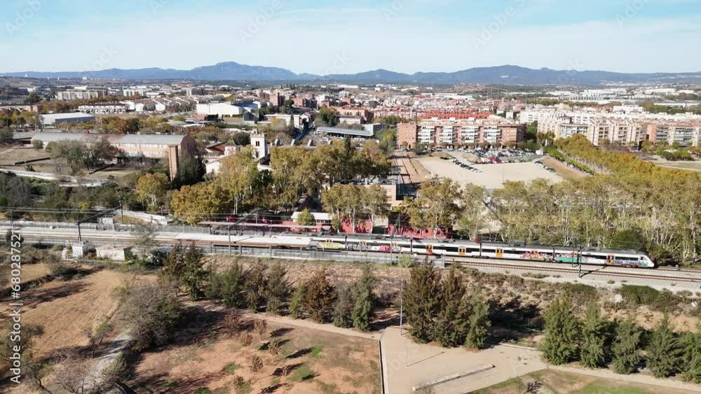 Trenes Renfe R2 Rodalies entrando y saliendo de la estación de Santa Perpètua de Mogoda, con vistas a Montserrat y al lago de Parc Central y un partido de fútbol, grabado desde dron 4k 60fps.
