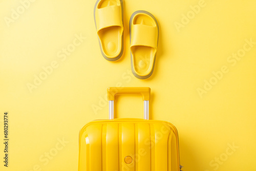 Vacation vibes captured: Overhead shot of a vibrant yellow suitcase, and rubber flip-flops on a sunlit yellow backdrop. Perfect for your travel-inspired message