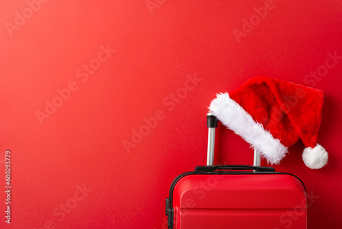 Explore the Winter Getaway idea. Overhead shot of stylish suitcase, and a Santa Claus hat, all on a vibrant red backdrop with space for text photo
