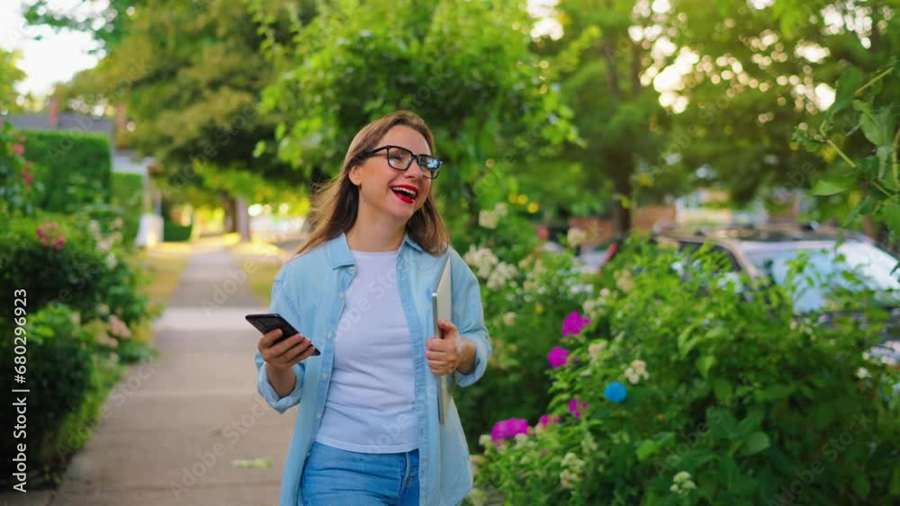 Woman with laptop and smartphone going in the blooming garden