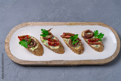 Sandwiches with anchovies and tomato on a white plate and on a concrete table. View from above.