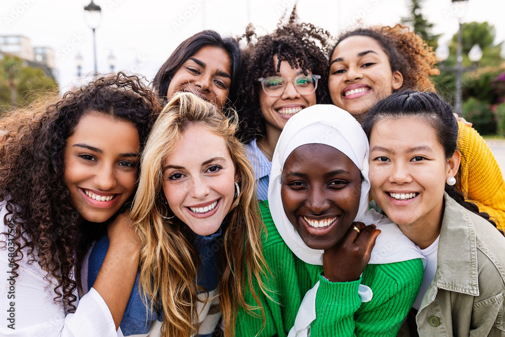 United portrait of young multiracial girls smiling at camera standing together outdoors. Millennial female friends feeling hugging each other smiling and posing for a photo. Women community concept. - obrazy, fototapety, plakaty 