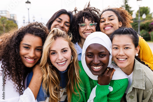 United portrait of young multiracial girls smiling at camera standing together outdoors. Millennial female friends feeling hugging each other smiling and posing for a photo. Women community concept. photo