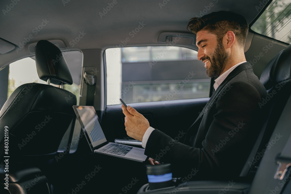 Handsome businessman in suit using personal computer and using mobile phone in taxi - obrazy, fototapety, plakaty 