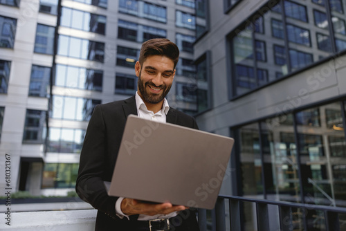 Stylish smiling male manager working on laptop standig on office terrace. High quality photo
