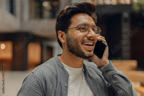 Smiling male manager in eyeglasses is talking phone standing in modern coworking space