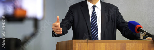 A man - a lawyer, politician or official - gestures while speaking from the podium in front of a microphone. Speaker, orator or rapporteur. Photo. Selective focus. No face