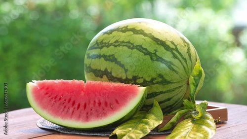 Giant Seedless Watermelon in wooden basket on wooden table in garden, Fresh Watermelon with slices on blurred greenery background.