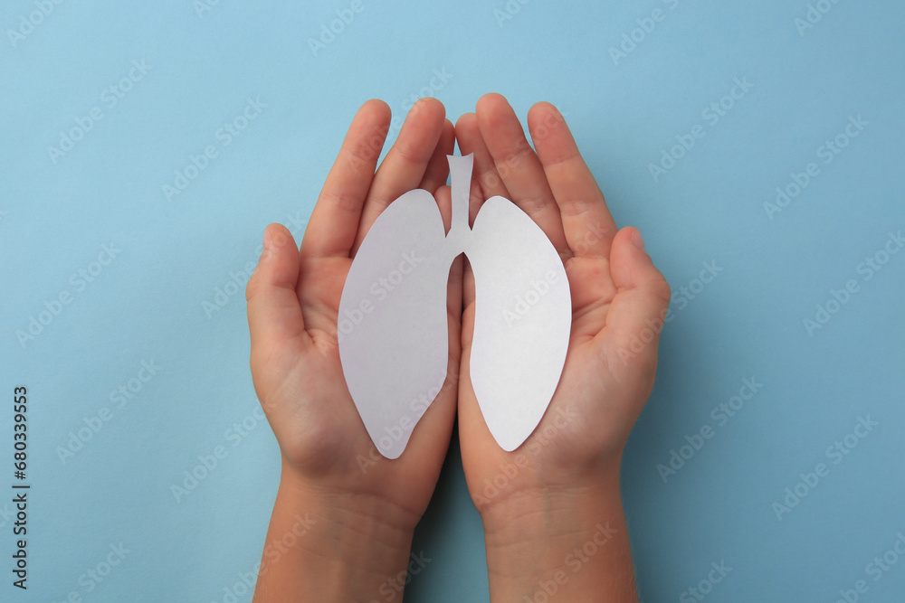 Child holding paper human lungs on light blue background, top view Child holding paper human lungs on light blue background, top view