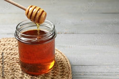 Pouring tasty honey from dipper into glass jar at grey wooden table, closeup. Space for text