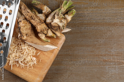 Grated horseradish and roots on wooden table, flat lay. Space for text