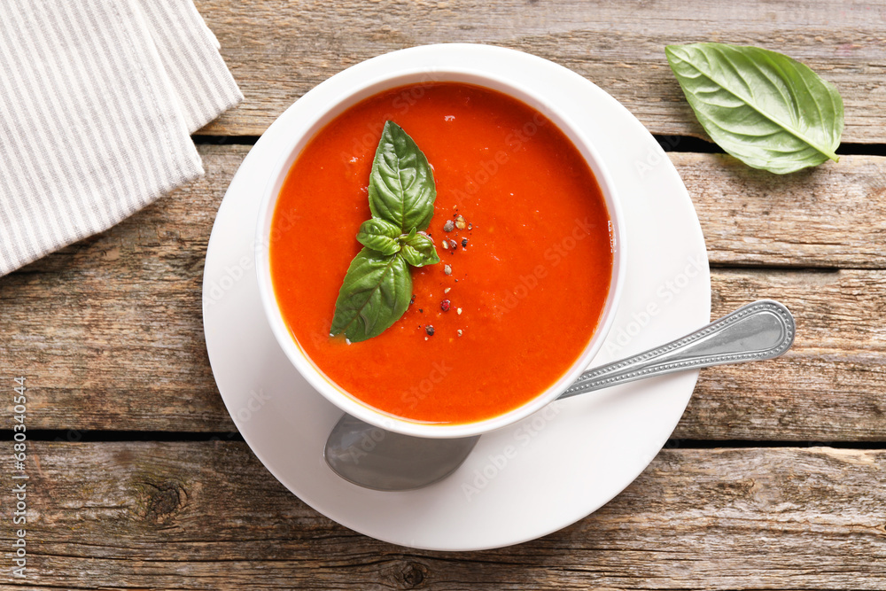 Delicious tomato soup with basil, spices and spoon on wooden table, flat lay Delicious tomato soup with basil, spices and spoon on wooden table, flat lay