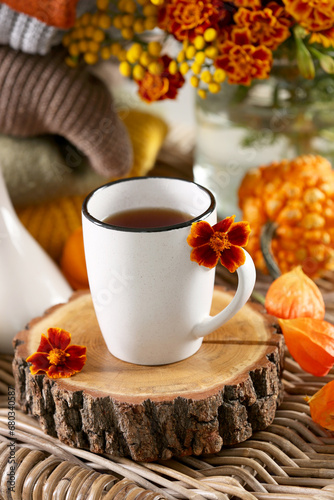 Cup of drink and autumn flowers on wicker table