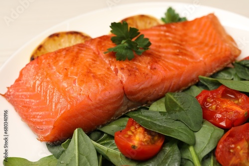Tasty grilled salmon with basil and tomatoes on white plate, closeup