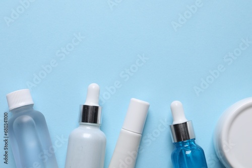 Many bottles and tube of cosmetic serum on light blue background, flat lay. Space for text