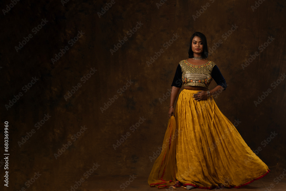 girl wearing indian wear - black blouse and yellow lehenga and dupatta beautiful makeup holding flowers in her hand in black background girl wearing indian wear - black blouse and yellow lehenga and dupatta beautiful makeup holding flowers in her hand in black background