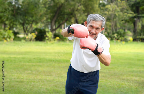 asian senior man with grey hair wears boxing gloves enjoy boxing exercise in the summer park concept of elderly people health recreation