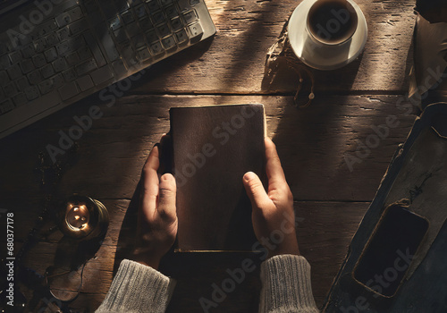 hands holding bible on old wood table with candle drink old computer keyboard and smart phone top view