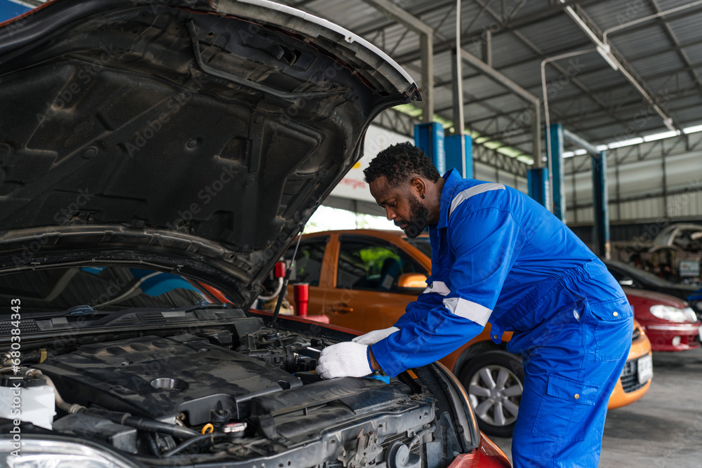 Mechanic working under the hood at the repair garage. Portrait of a happy mechanic man working on a car in an auto repair shop. Male mechanic working on car.