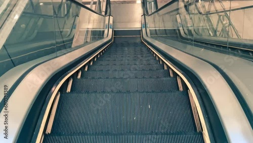 Close-up of an empty escalator going down. The steps were clean and shiny, and the handrails were smooth and smooth. The metal railings on both sides of the escalator are painted dark grey