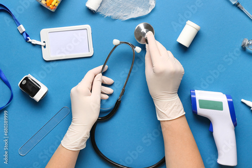 Doctor with stethoscope and medical supplies on blue background, top view
