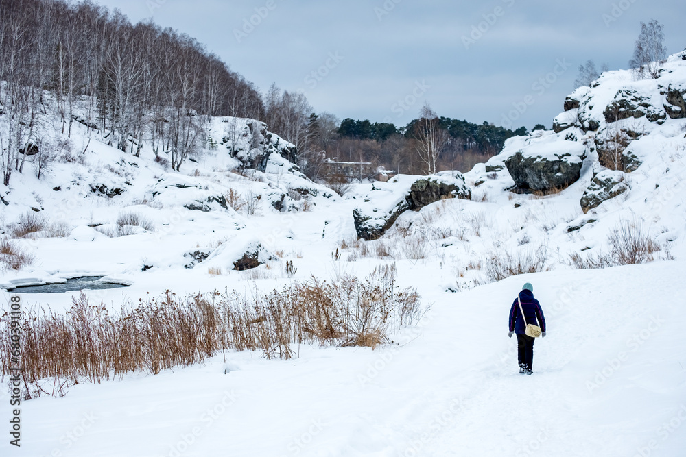 a girl walks away from us along a frozen winter river, a winter landscape and a girl leaving with a bag
