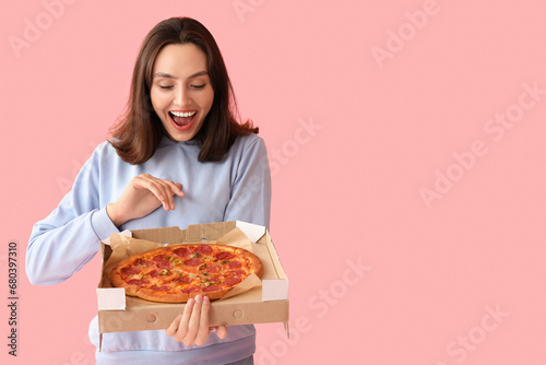 Happy young woman holding cardboard box with tasty pizza on pink background