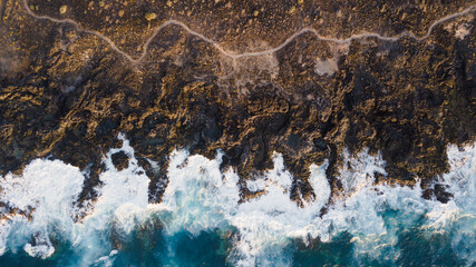 Drone view of Tenerife south coast with Atlantic ocean and strong swell beating against the walls of a rocky cliff, blue rough sea with big waves with foam crashing against the rocks